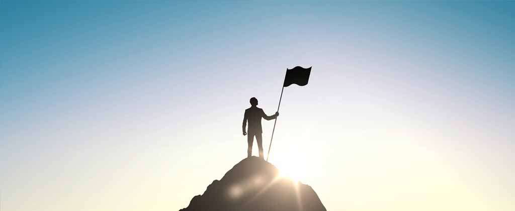 Homem chega ao topo de uma montanha e finca sua bandeira