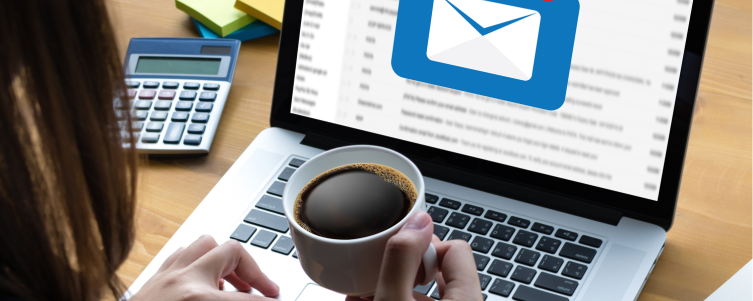 Mulher segura xícara de café enquanto acessa os e-mails no notebook