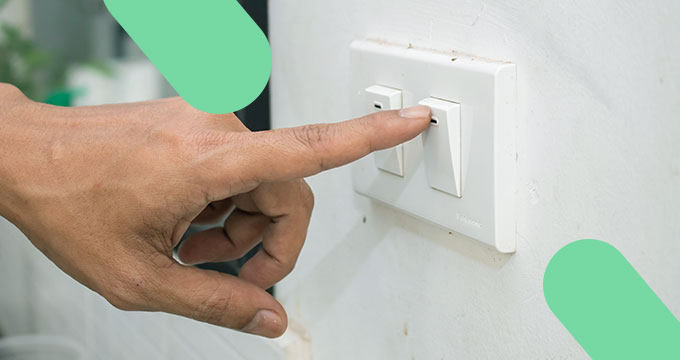 Mão apagando a luz ilustrando maneiras de economizar em casa