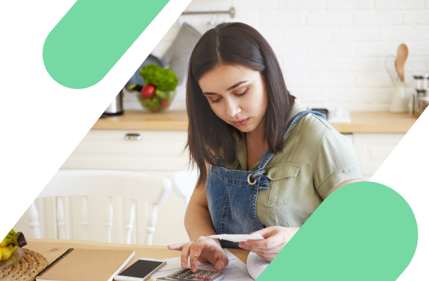 Como negociar o aluguel: mulher na cozinha de casa fazendo contas na calculadora pra descobrir quanto vai precisar negociar do seu aluguel